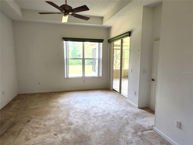 carpeted empty room with ceiling fan, a textured ceiling, and a tray ceiling