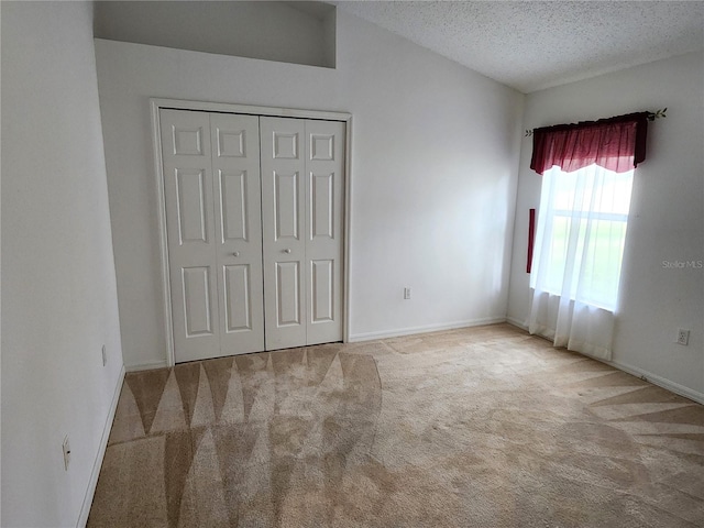 unfurnished bedroom featuring a closet, a textured ceiling, carpet, and lofted ceiling