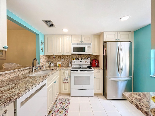 kitchen with backsplash, white appliances, light tile floors, and light stone countertops