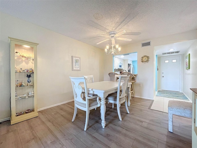 dining area with hardwood / wood-style floors, ceiling fan with notable chandelier, and a textured ceiling