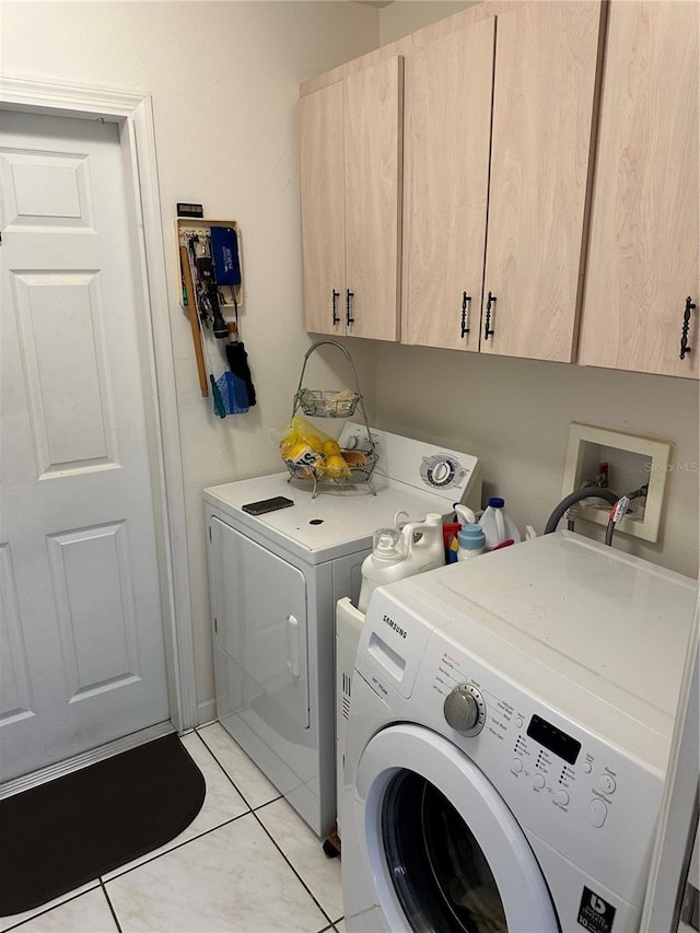 clothes washing area featuring washing machine and clothes dryer, light tile patterned floors, and cabinets