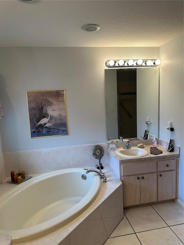 bathroom with tiled tub, tile patterned flooring, vanity, and a textured ceiling