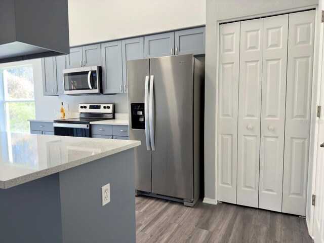 kitchen featuring stainless steel appliances, dark wood-type flooring, gray cabinetry, and light stone counters