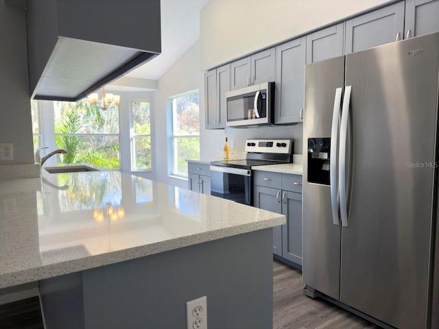 kitchen with lofted ceiling, hardwood / wood-style flooring, gray cabinets, stainless steel appliances, and light stone countertops