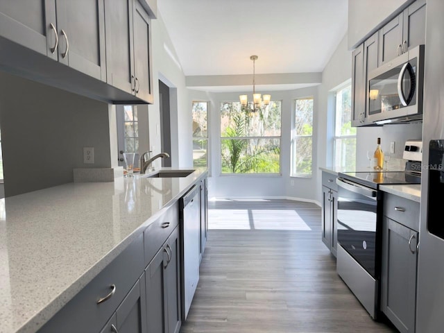 kitchen featuring decorative light fixtures, sink, gray cabinetry, light stone counters, and stainless steel appliances