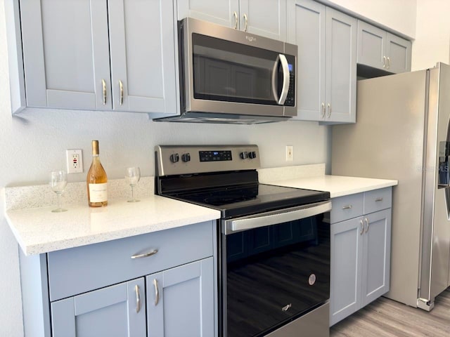 kitchen with light stone counters, light hardwood / wood-style flooring, stainless steel appliances, and gray cabinets