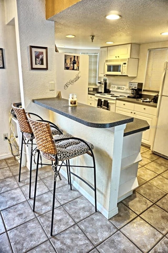 kitchen featuring a kitchen breakfast bar, kitchen peninsula, white appliances, light tile floors, and white cabinets