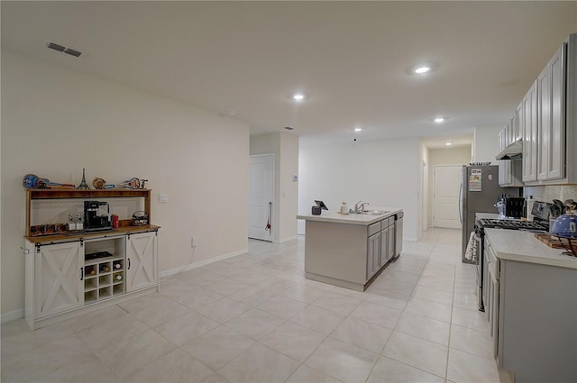 kitchen featuring a center island with sink, gray cabinets, light tile floors, sink, and appliances with stainless steel finishes