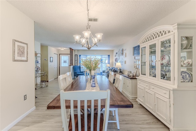 dining room featuring a textured ceiling, light wood-type flooring, and an inviting chandelier