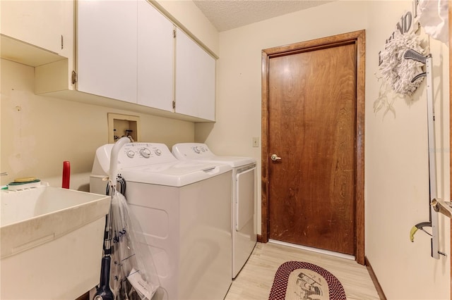 clothes washing area featuring cabinets, light wood-type flooring, a textured ceiling, sink, and separate washer and dryer