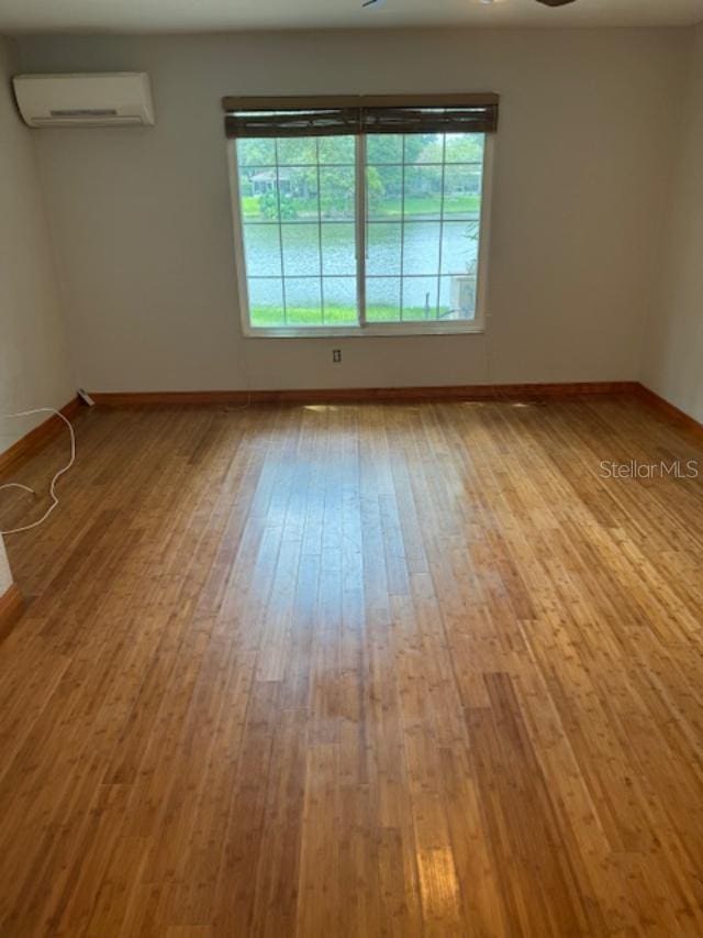 unfurnished room with a wall unit AC, light hardwood / wood-style flooring, and ceiling fan