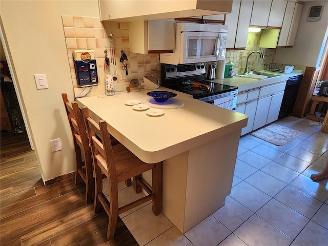 kitchen featuring backsplash, a kitchen bar, electric range, and kitchen peninsula