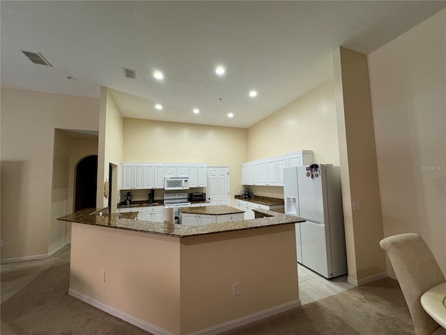 kitchen featuring white appliances, light carpet, white cabinets, a spacious island, and dark stone countertops