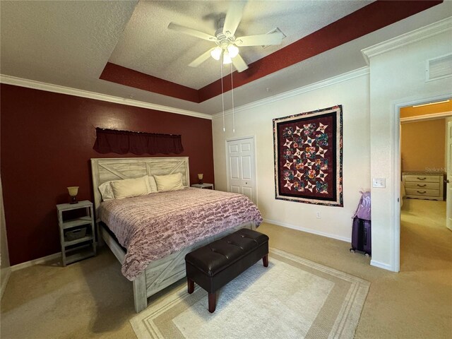 bedroom featuring ceiling fan, ornamental molding, a tray ceiling, light colored carpet, and a closet