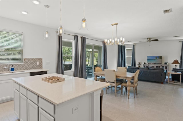 kitchen featuring tasteful backsplash, decorative light fixtures, light tile flooring, a kitchen island, and white cabinets