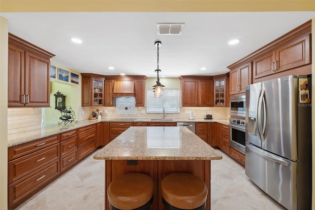 kitchen with appliances with stainless steel finishes, a kitchen breakfast bar, sink, pendant lighting, and a kitchen island