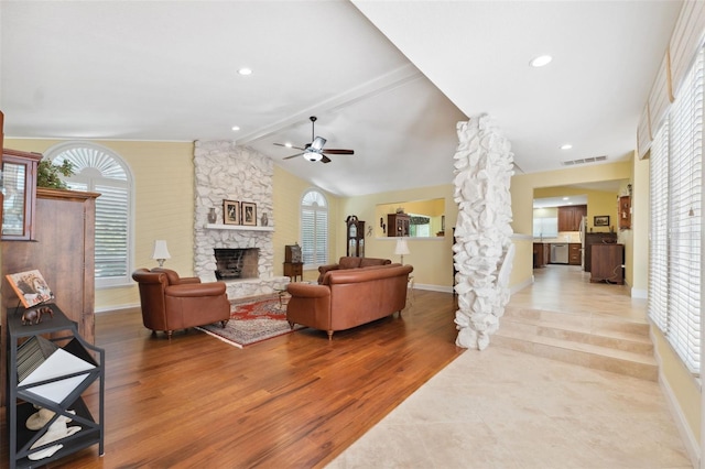 living room with hardwood / wood-style floors, lofted ceiling with beams, ceiling fan, and a stone fireplace