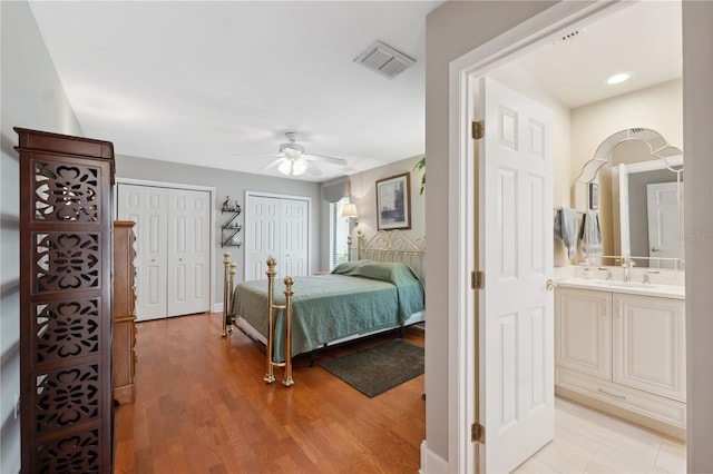 bedroom with sink, ceiling fan, light wood-type flooring, connected bathroom, and multiple closets