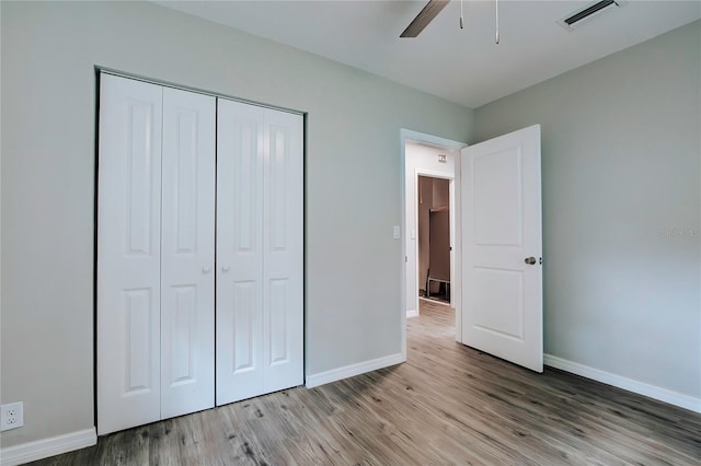 unfurnished bedroom with a closet, wood finished floors, visible vents, and baseboards
