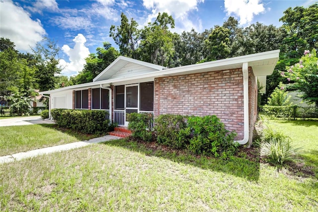 ranch-style home with an attached garage, a sunroom, a front yard, and brick siding