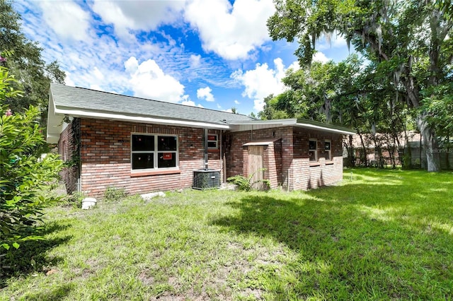 rear view of property featuring a lawn, brick siding, and central AC unit