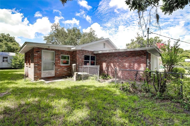 rear view of house featuring brick siding, a lawn, and fence