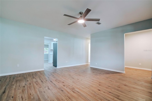 empty room with light wood finished floors, baseboards, a ceiling fan, and visible vents
