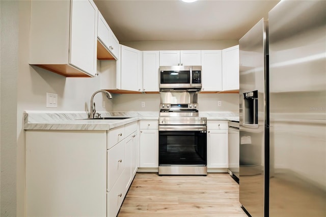 kitchen with light countertops, a sink, light wood-style flooring, appliances with stainless steel finishes, and white cabinetry