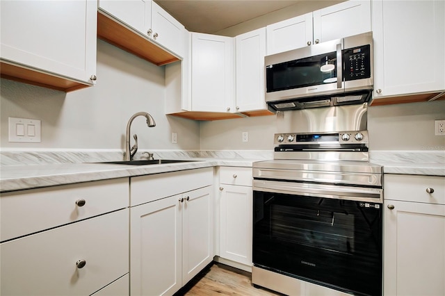 kitchen with white cabinetry, light stone countertops, light hardwood / wood-style floors, stainless steel appliances, and sink