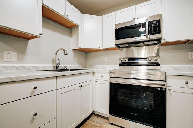 kitchen with a sink, light wood-type flooring, white cabinetry, light stone counters, and appliances with stainless steel finishes