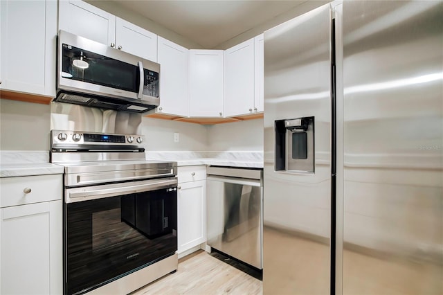 kitchen with white cabinets, light stone counters, light wood-style floors, and appliances with stainless steel finishes