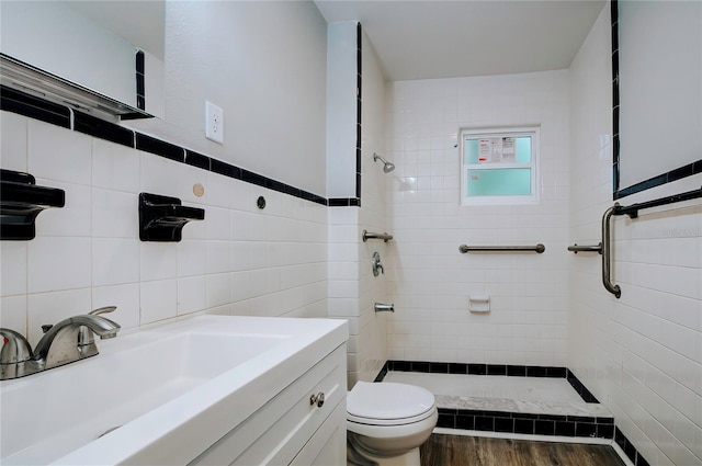 bathroom with a tile shower, toilet, tile walls, wood-type flooring, and vanity