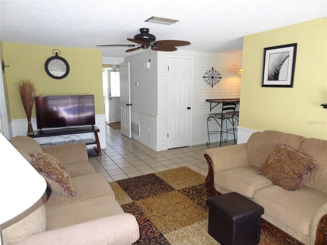 living room featuring ceiling fan, light tile patterned floors, a textured ceiling, and brick wall