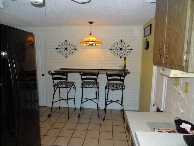 kitchen with pendant lighting, black fridge, light tile patterned floors, a textured ceiling, and brick wall