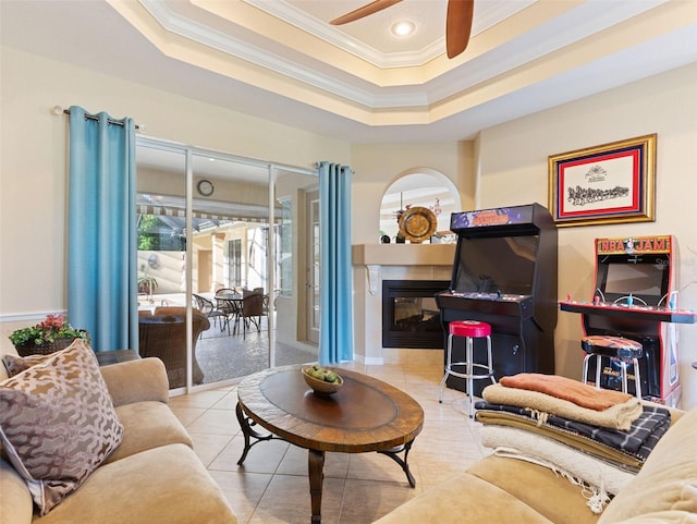 tiled living room with a raised ceiling, ceiling fan, and ornamental molding