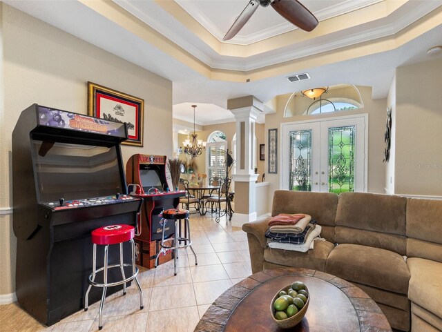 tiled living room featuring french doors, ornate columns, ornamental molding, ceiling fan with notable chandelier, and a tray ceiling