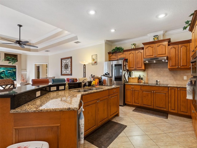 kitchen with stainless steel refrigerator, sink, an island with sink, a tray ceiling, and ornamental molding