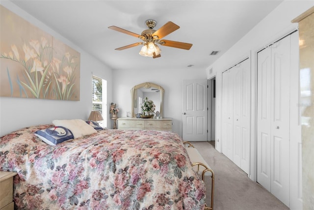 carpeted bedroom featuring multiple closets and ceiling fan