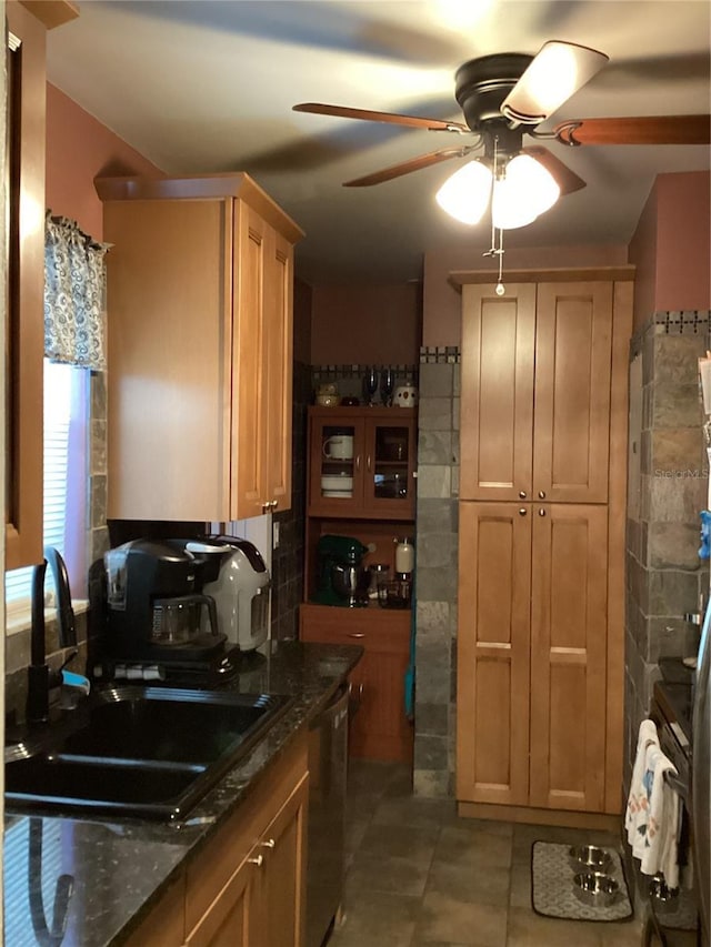 kitchen with stainless steel dishwasher, ceiling fan, sink, dark stone countertops, and tile patterned flooring