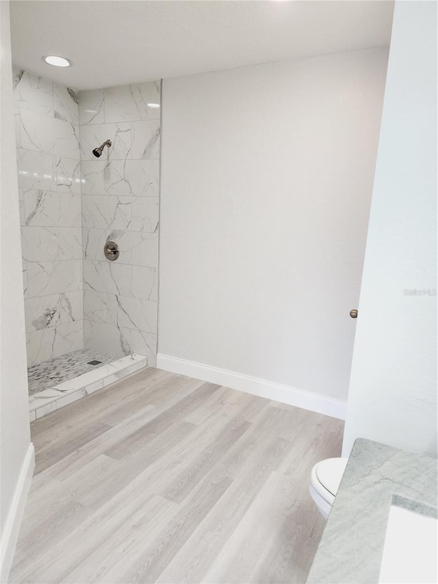 bathroom featuring a tile shower, hardwood / wood-style flooring, and toilet