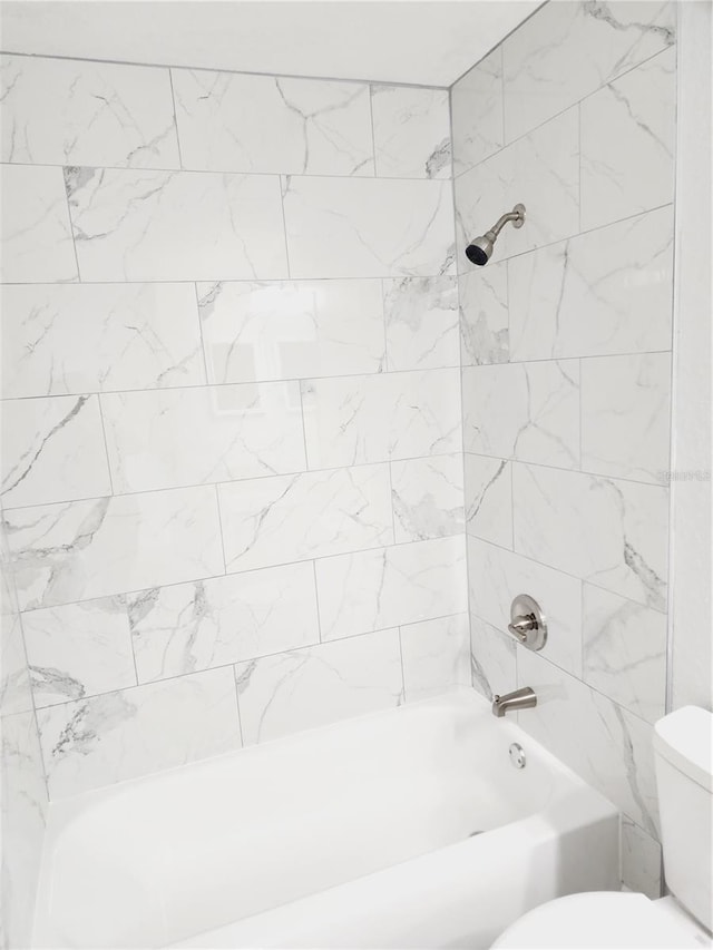 bathroom featuring tiled shower / bath combo and toilet