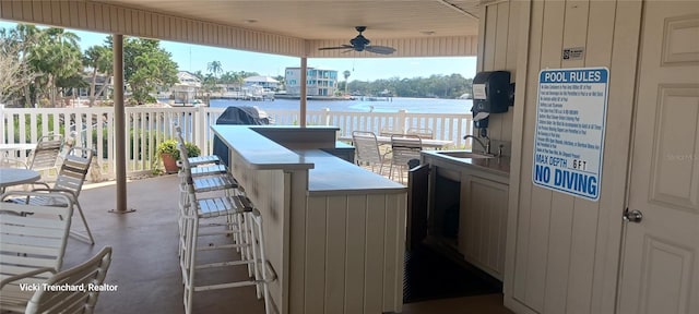 view of patio / terrace featuring a water view, ceiling fan, and an outdoor wet bar