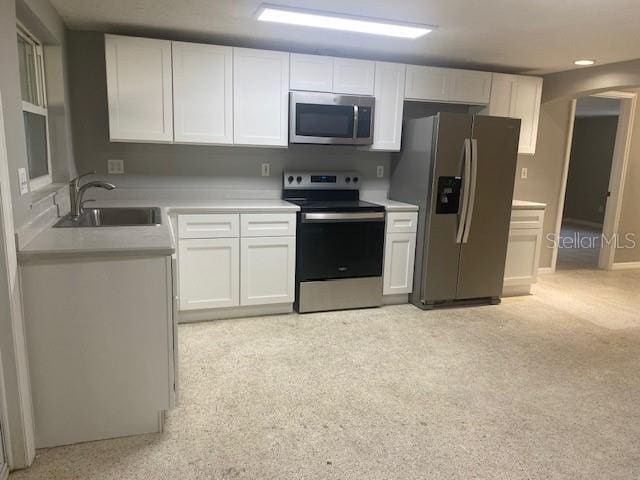 kitchen with white cabinetry, sink, stainless steel appliances, and light carpet