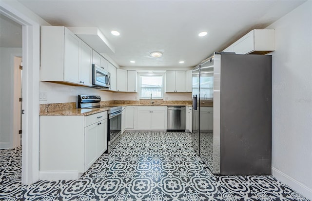 kitchen with light stone countertops, appliances with stainless steel finishes, white cabinets, sink, and light tile flooring