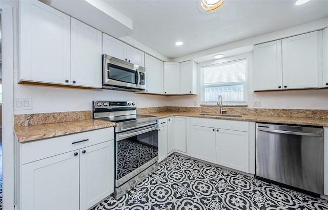 kitchen with white cabinetry, light stone countertops, stainless steel appliances, sink, and light tile floors