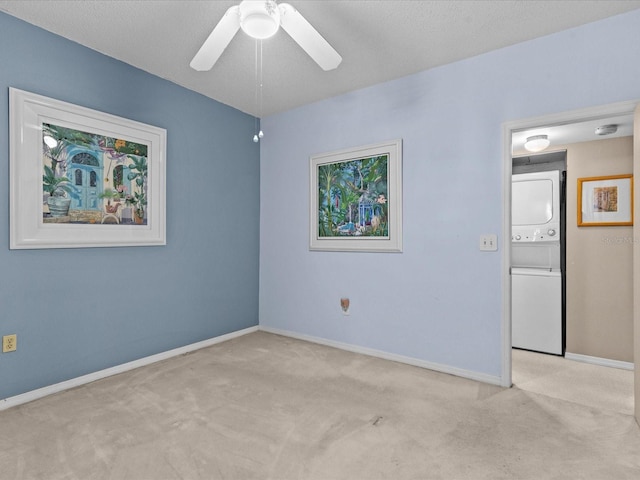 unfurnished room featuring a ceiling fan, stacked washer and clothes dryer, light carpet, and baseboards