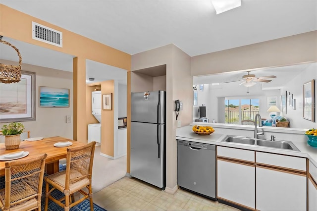 kitchen featuring light countertops, appliances with stainless steel finishes, white cabinetry, a sink, and stacked washing maching and dryer