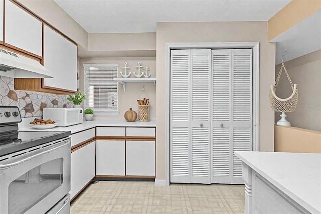 kitchen featuring electric stove, white microwave, light countertops, and white cabinetry