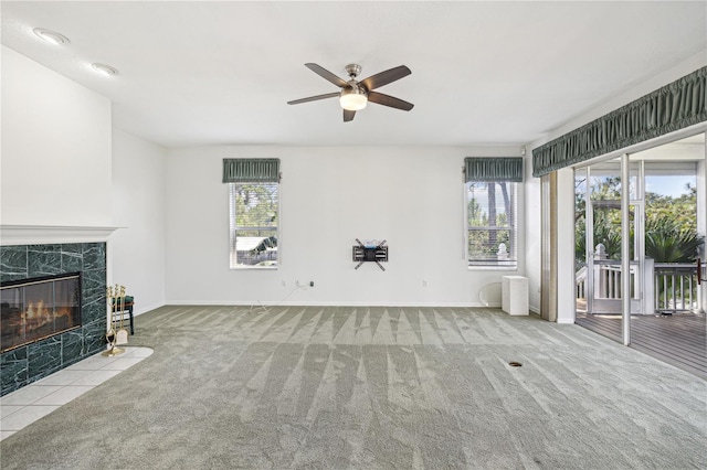 unfurnished living room featuring ceiling fan, light colored carpet, a tile fireplace, and a wealth of natural light