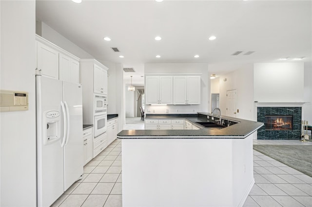 kitchen featuring kitchen peninsula, white appliances, sink, light tile patterned floors, and white cabinetry